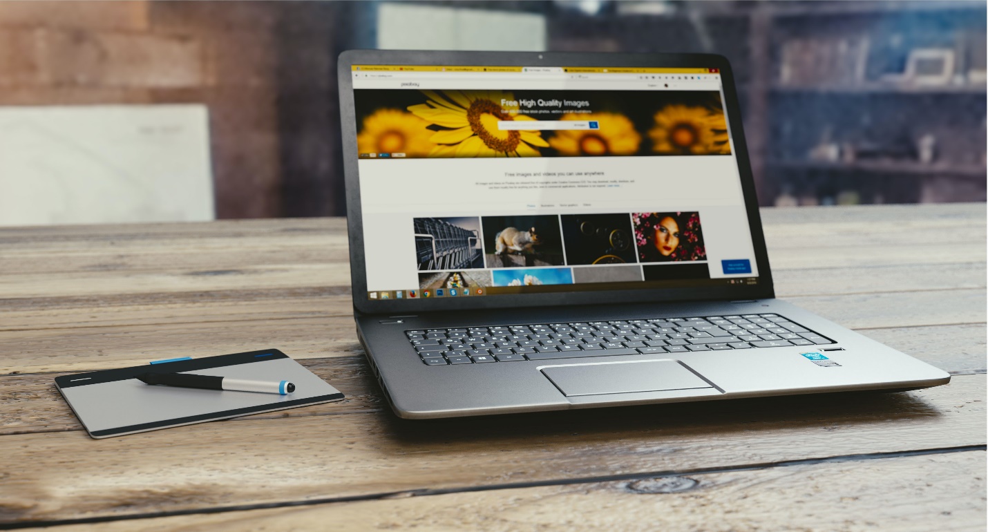 A laptop displays a website as a pen and paper sit closeby on a wooden table